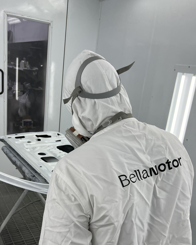 Bella Motor painter in branded overalls in the paint booth