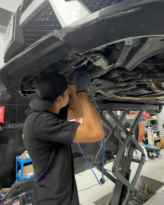 Technician working under a car on the lift at Bella Motor
