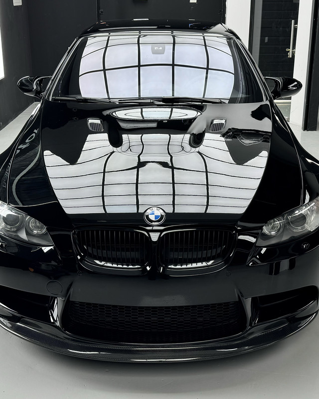 High-gloss black BMW M3 reflecting the workshop lights