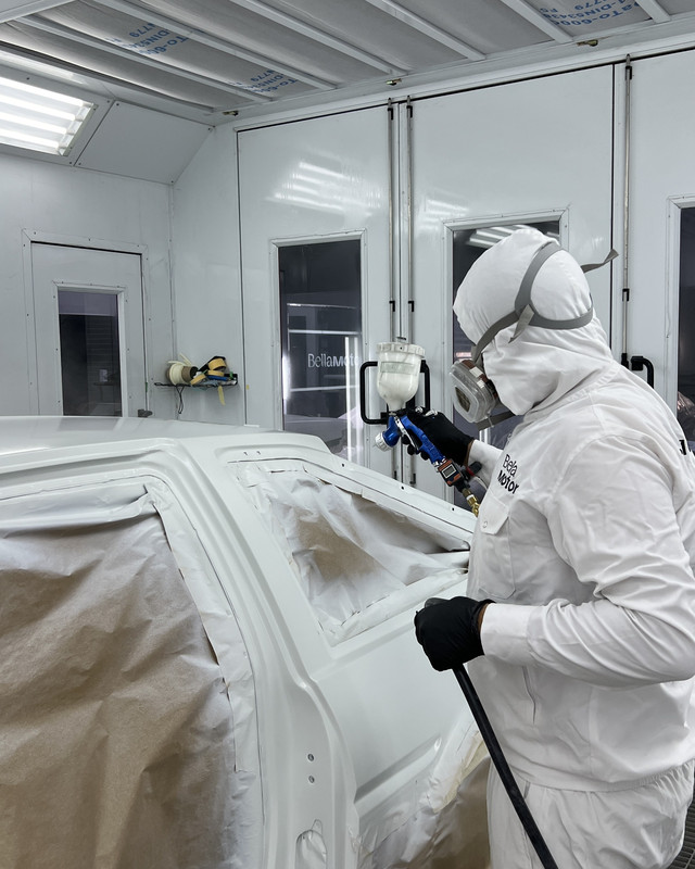 Painter spraying a full car in the Bella Motor paint booth