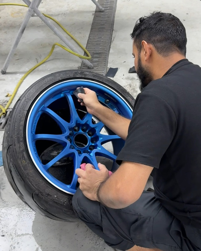 Technician refinishing a blue alloy wheel